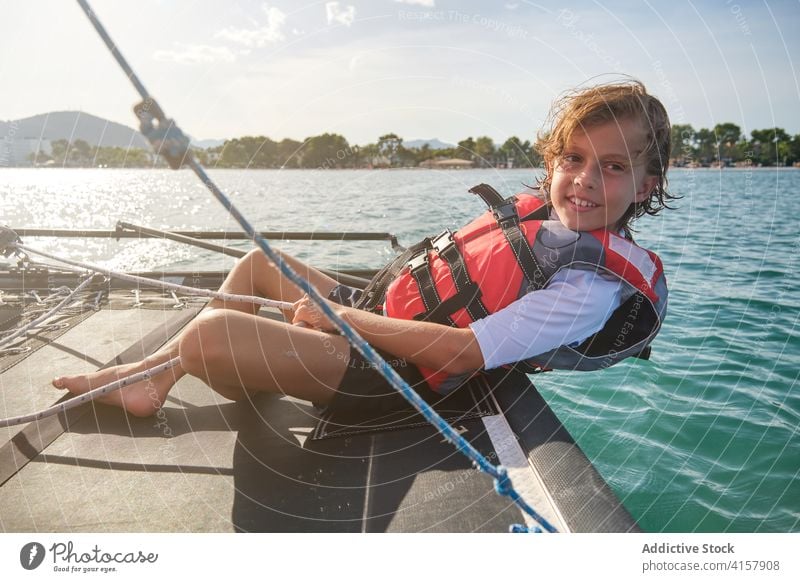 Boy with life jacket leaning on the edge of a boat holding the rudder and a rope in the sea sailing weight seashore driving enjoyment vacations child sailboat