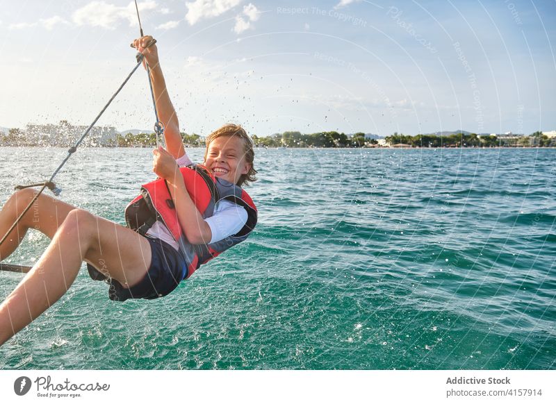 Water drops splashing a kid with a life jacket hanging from a rope of a boat on the sea freedom counterweight laugh gesture racing assistance way wind balance