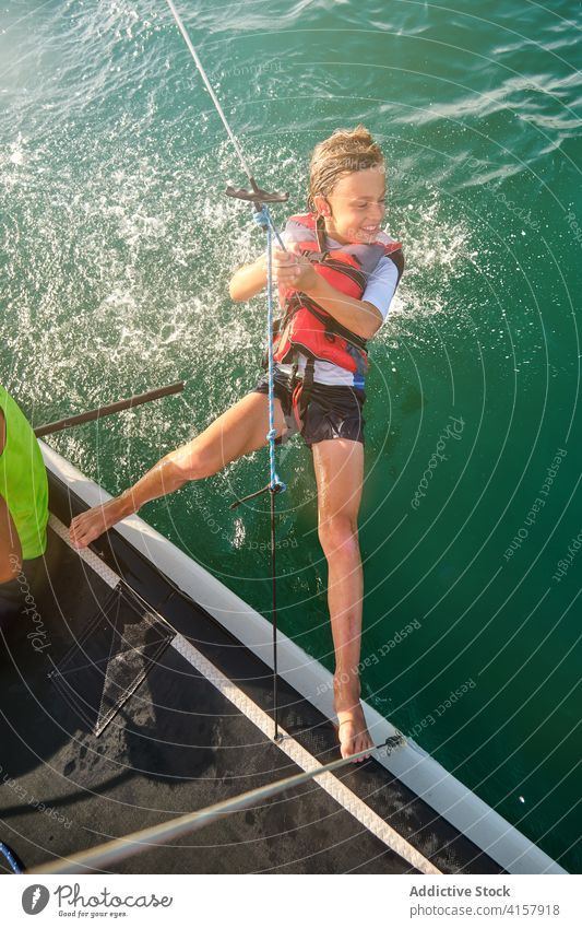 Boy with life jacket hanging from a rope sailing in the sea with a boat racing assistance gesture weight splash way wind responsibility balance enjoyment future