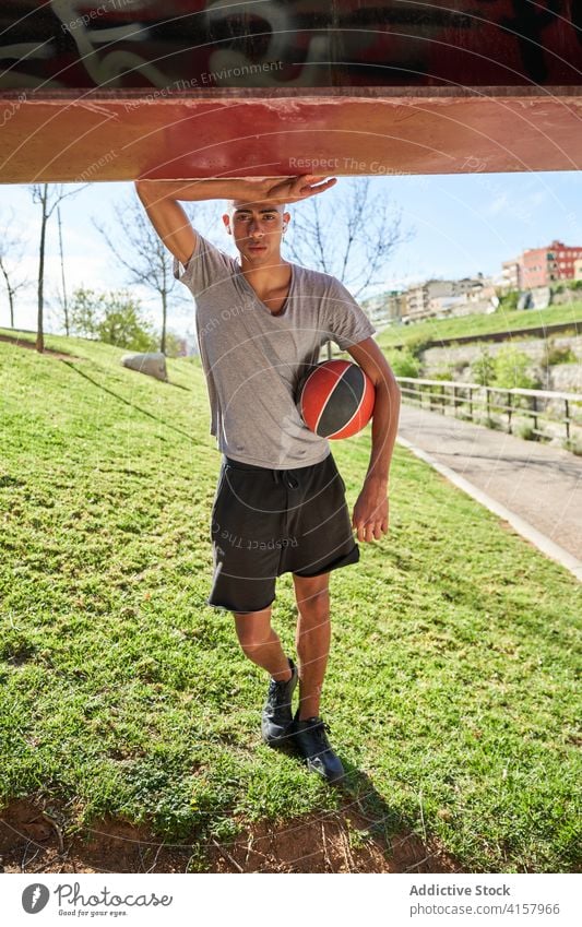 Sporty man with ball standing in park sportsman training young athlete workout confident exercise ethnic male determine sportswear fitness streetball basketball