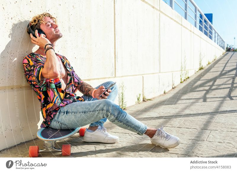 Relaxed male skater listening to music in city man relax enjoy urban trendy hipster headphones skateboard street dreamy eyes closed modern rest cool young guy