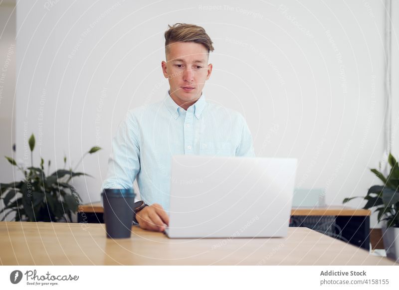Focused man using laptop in workplace freelance entrepreneur busy startup takeaway coffee workspace male wooden table device gadget job internet remote project