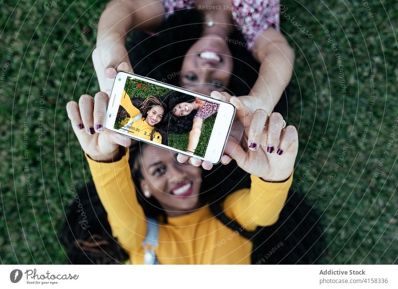Delighted African American women taking selfie on grass friendship best friend smartphone lying together charming ethnic black african american green cheerful