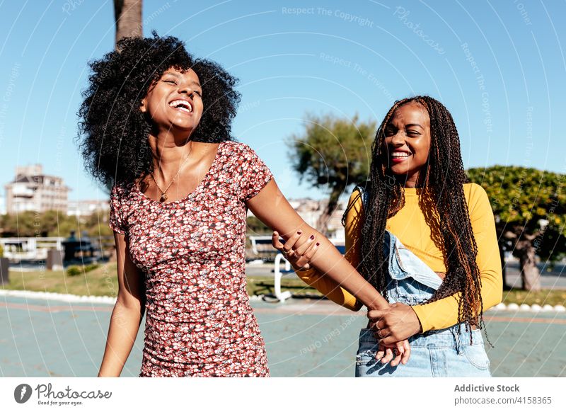 Smiling black women walking along street together friend tropical holding hands delight friendship best friend summer ethnic african american happy town