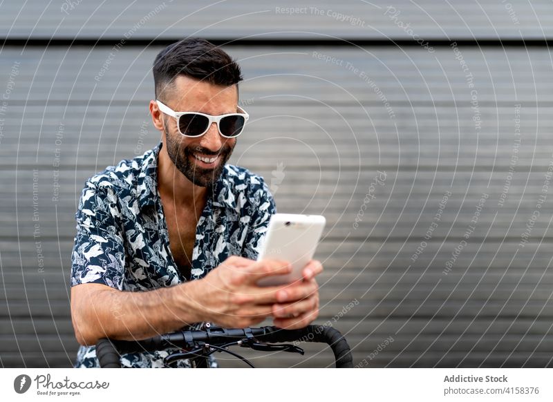 Cheerful man using smartphone on street social media city bicycle bike lean trendy style male masculine handsome mobile handlebar outfit browsing gadget online