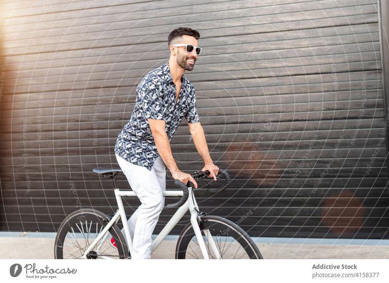Smiling man riding bicycle on street ride rider cyclist style trendy city cheerful male handsome masculine hobby modern bike weekend casual urban town summer