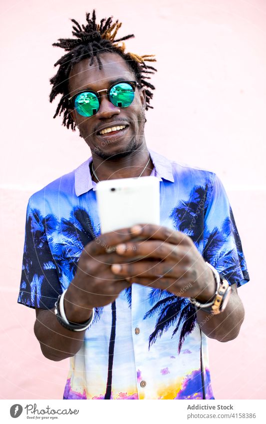 Stylish black man using smartphone in city tropical shirt style outfit trendy appearance social media male ethnic african american print dreadlocks building