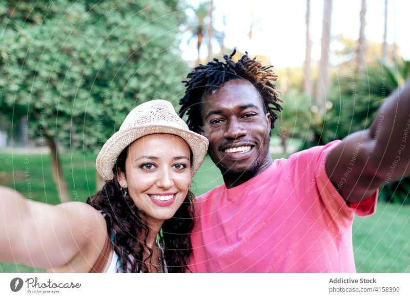 Smiling multiethnic couple taking selfie in park travel smartphone moment enjoy adventure wanderlust using multiracial diverse black african american green
