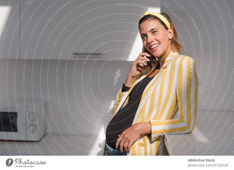 Stylish pregnant woman talking on phone in kitchen home smartphone call style trendy modern young female stripe yellow device gadget lifestyle speak mobile