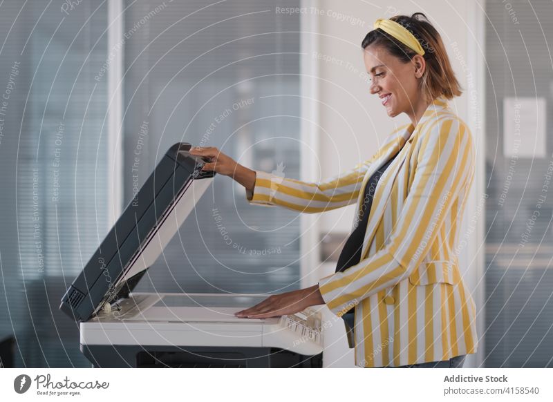 Positive pregnant businesswoman using photocopier work scanner machine xerox copy document paper workspace cheerful smile occupation entrepreneur contemporary