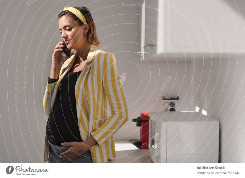 Stylish pregnant woman talking on phone in kitchen home smartphone call style trendy modern young female stripe yellow device gadget lifestyle speak mobile