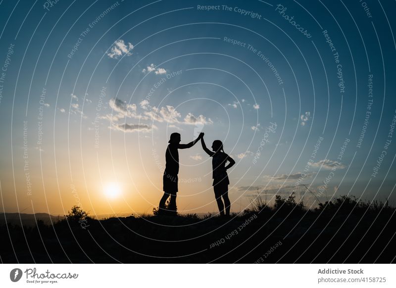 Active couple enjoying sunset in mountains friend high-fiving hill silhouette skyline sundown happy active together nature adventure freedom hike twilight dusk