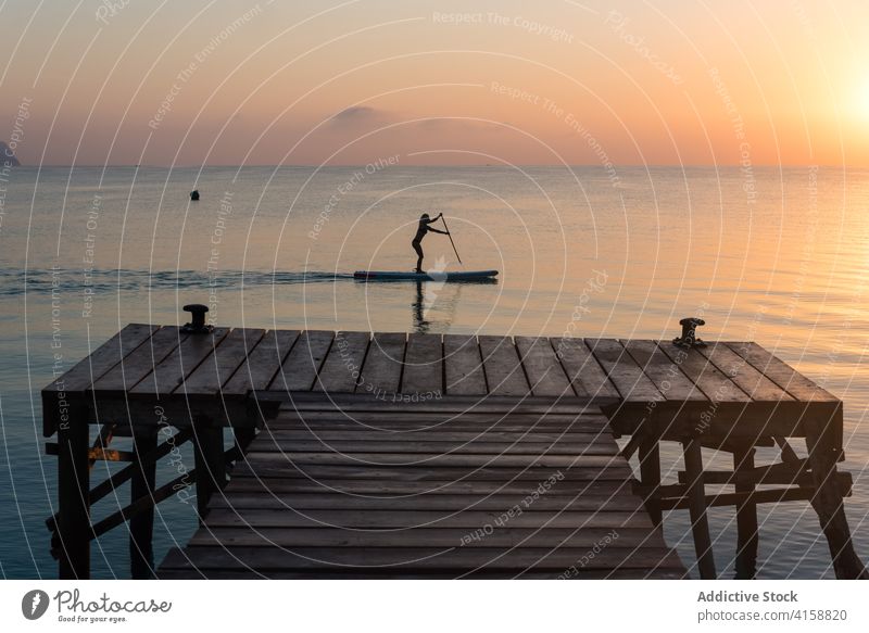 Woman rowing on paddleboard in sea surfer woman silhouette sunset practice female training sup board surfboard summer sporty stand calm water sundown sky