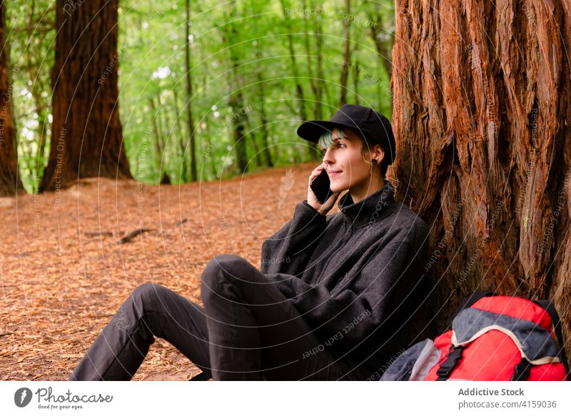 Smiling traveler talking phone in forest woman smartphone explore woods greeting female natural monument of sequoias cantabria spain call tree tourist gadget