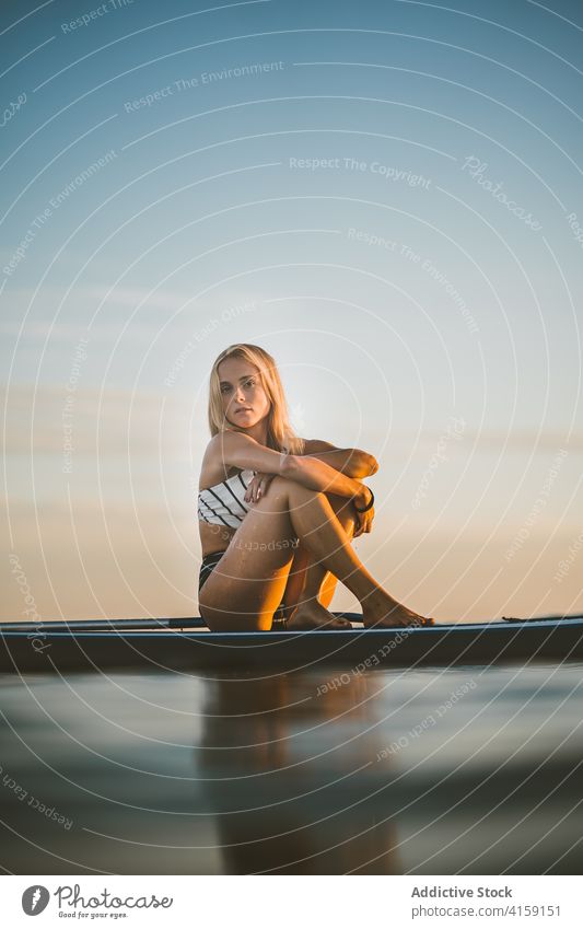 Carefree woman on paddleboard in sea relax sunset sup surfboard slim sundown female swimsuit ocean summer sit rest enjoy holiday nature fit sky tranquil evening