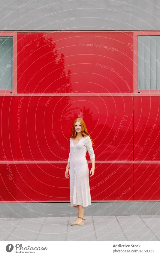 Stylish young woman standing near red wall modern urban style dress red hair trendy fashion color bright female redhead ginger contemporary lady lifestyle vivid
