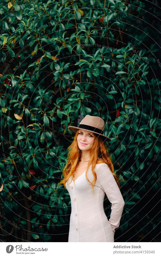Young woman in hat standing in garden style redhead trendy red hair modern ginger vogue young female fashion long hair lady confident charming lifestyle elegant