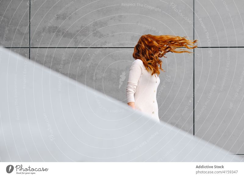 Ginger woman with flying hair standing near wall redhead ginger wind urban style long hair modern female red hair trendy color mystery contemporary elegant