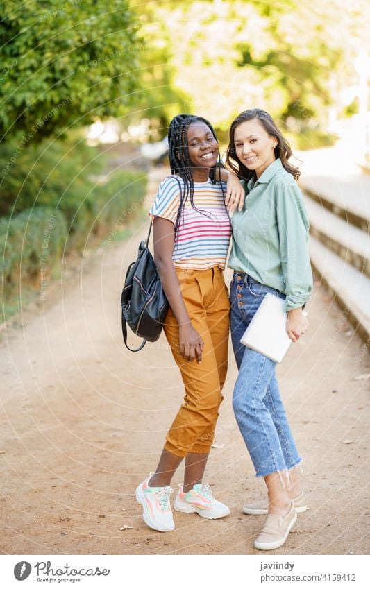 Two multiethnic women posing together with colorful casual clothing woman friend tablet digital female girl young lifestyle urban beautiful device outside lady