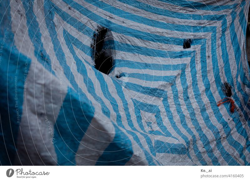 Blue and white striped tarpaulin with large holes serves as visual and weather protection Inspiration Deserted Colour photo Available light Exterior shot Detail