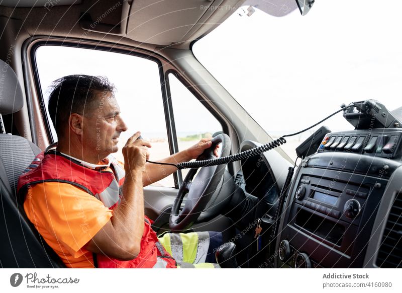 Ambulance worker driving vehicle while talking on radio transceiver ambulance driver walkie talkie communicate uniform steering wheel inside speak man panel