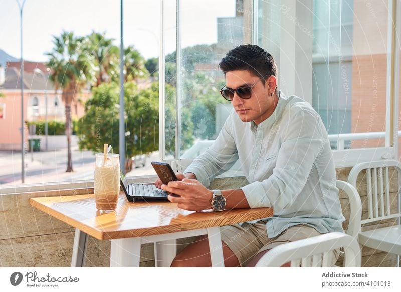 Focused young man working distantly using laptop and smartphone freelance focus online connection internet male style concentrate cafe gadget job entrepreneur