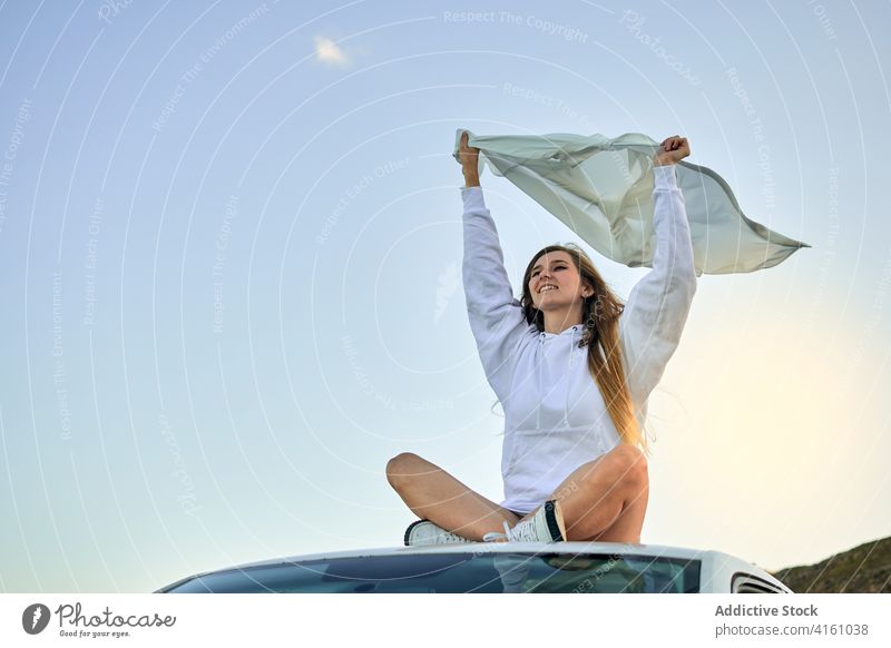 Tranquil woman on car roof with fluttering cloth wind traveler freedom carefree enjoy female automobile piece sit journey adventure serene vacation rest tourism