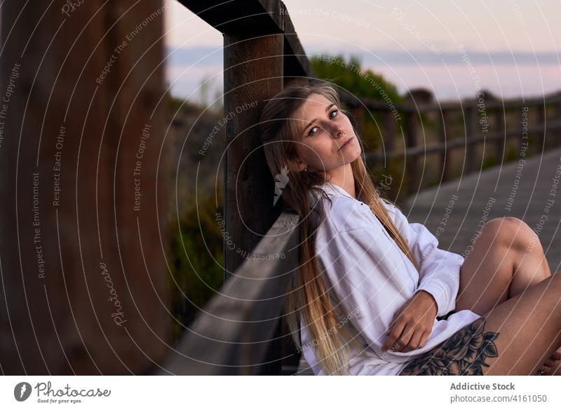Peaceful woman relaxing on promenade at sundown dreamy traveler sunset carefree calm evening female embankment wooden fence lean nature looking at camera