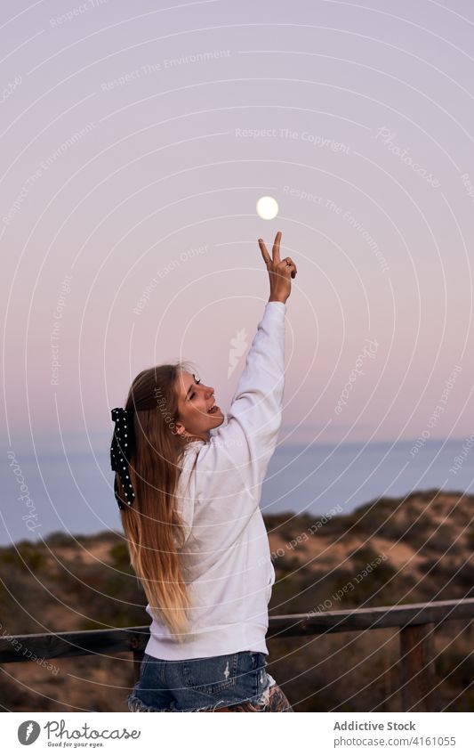 Carefree woman showing two fingers against sunset sky peace sign carefree v sign promenade traveler female cheerful happy vacation stand holiday freedom evening