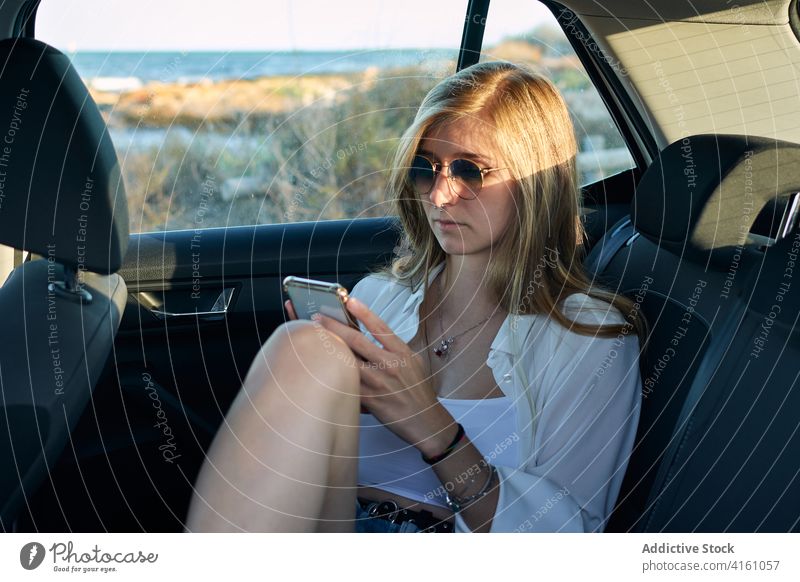 Tranquil woman using smartphone in car relax road trip adventure wanderlust carefree freedom female backseat traveler rest holiday device window cellphone