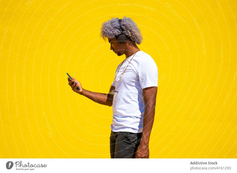 Black man with afro hair listening to music with earphones on a headphones black man music helmets playing music yellow background mobile dj black earphones