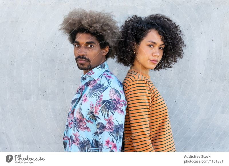 Multiethnic friends in stylish clothes near cement wall couple apparel hairstyle afro attentive friendship portrait gaze trendy partner look focus appearance