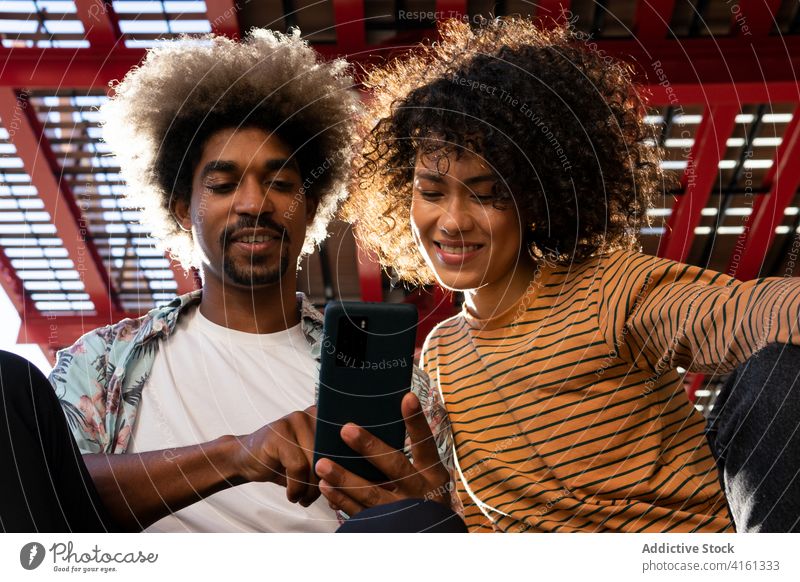 Cheerful black man sharing smartphone with ethnic friend couple watching share friendship smile internet online afro using gadget device hairstyle cellphone