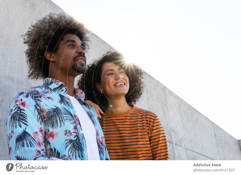 Multiethnic friends in stylish clothes near cement wall couple apparel hairstyle afro attentive friendship portrait gaze trendy partner look focus appearance