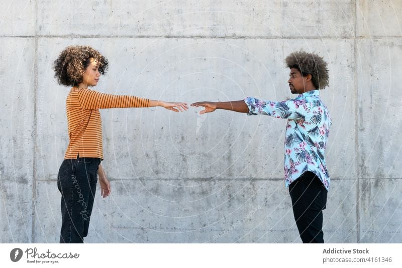 Joyful ethnic couple reaching out hands to each other on street reach out together relationship love against scial distancing relax city style rest concrete