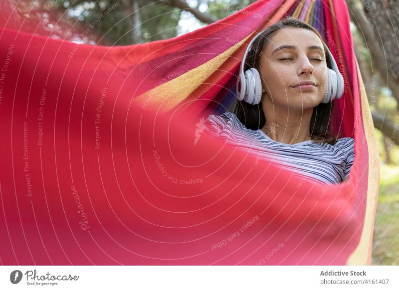 Carefree woman listening to music in hammock enjoy hang park wireless melody calm female headphones peaceful sound lying serene song harmony audio eyes closed