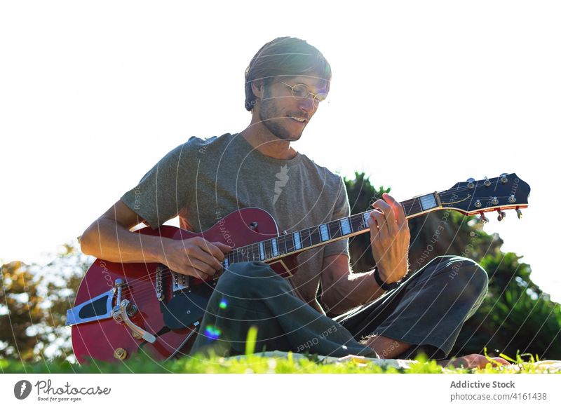 Man playing guitar in park man electric music musician instrument melody summer male sunny entertain grass hobby cheerful rest happy practice lawn song smile