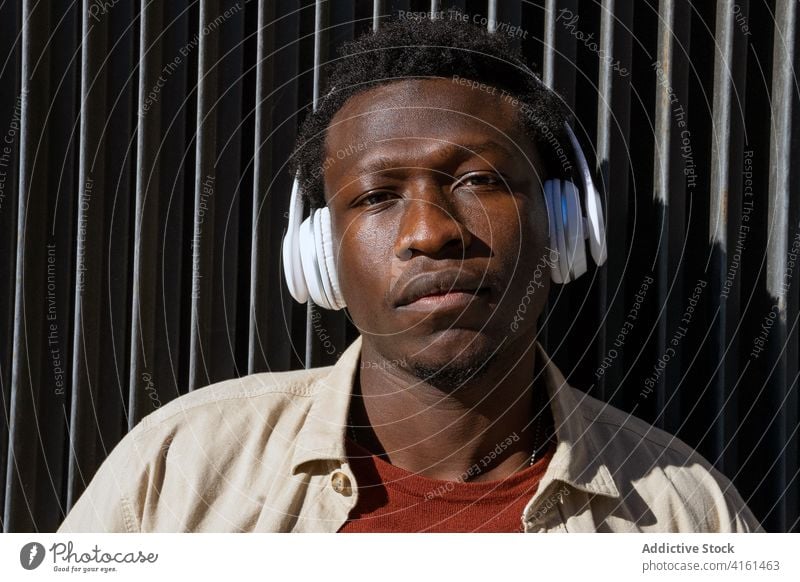 Black man in headphones in city listen music street calm wireless song melo male ethnic black african american metal wall lean urban sound modern gadget