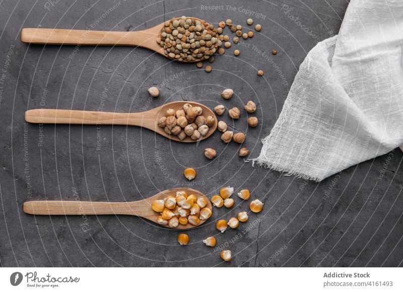 Various grains in wooden spoons on table crop pea chickpea corn dry dried row kitchen ingredient arrangement organic food cuisine scatter composition cutlery
