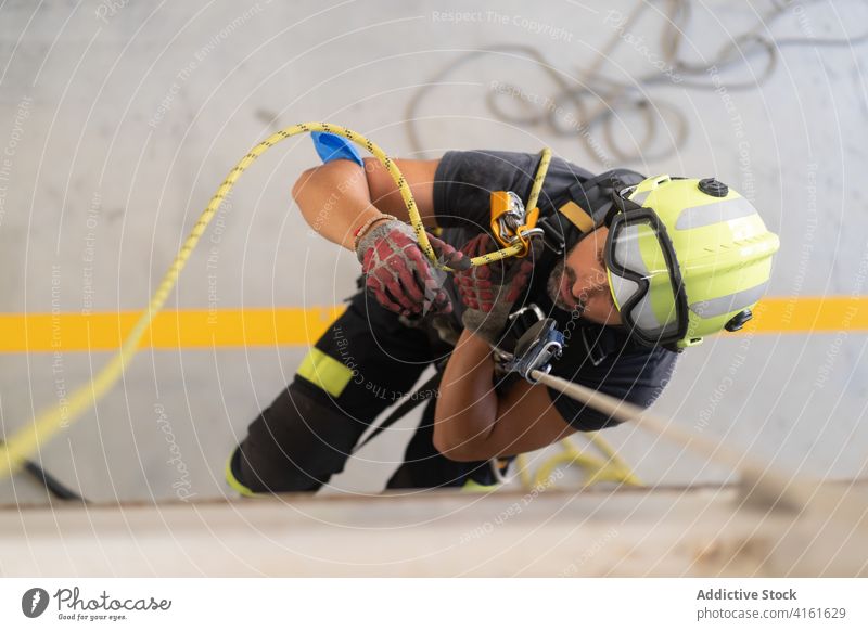Bearded firefighter in helmet climbing wall on rope at work routine practice professional safety protective skill fireman glove job floor prepare process