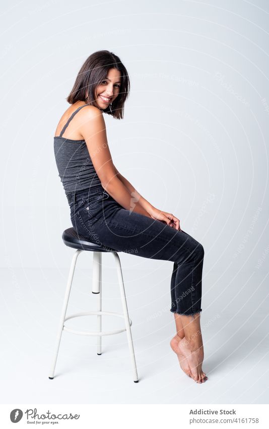 Cheerful woman sitting on stool in studio toothy smile joy excited cool appearance expressive gorgeous carefree cheerful attractive young slim chair trendy