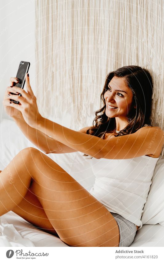 Positive young woman taking selfie in bedroom morning home cheerful smartphone happy share teen teenage millennial female gadget device social media using smile