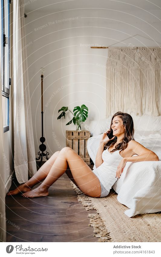 Happy woman talking on smartphone and leaning on bed phone call conversation charming speak cellphone smile bedroom content communicate gadget device using