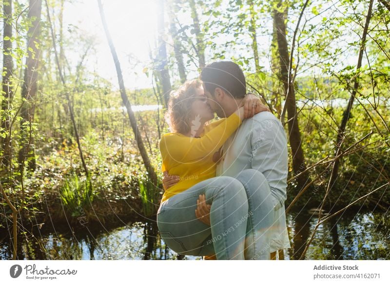 Happy couple kissing gently in nature carry romantic tender relationship park together love hug close touch embrace relax bonding boyfriend lake pond sunny