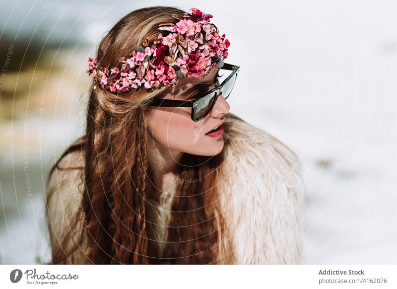 Stylish bohemian woman in fur jacket and sunglasses sitting in snowy woods style fashion nordic nature forest wreath season spring young female floral outfit