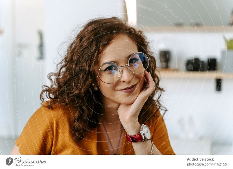 Happy young woman sitting at table with hand at chin positive smile style cheerful happy entrepreneur content glad joy female ginger hair curly hair casual