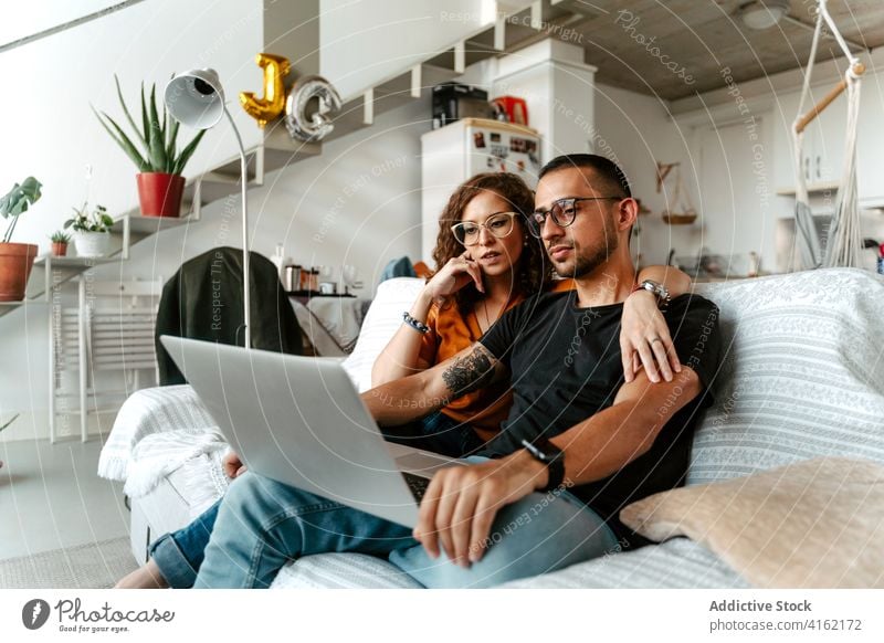 Serious young diverse couple watching film on laptop at home movie cuddle relax sofa love relationship together share using internet husband wife multiracial