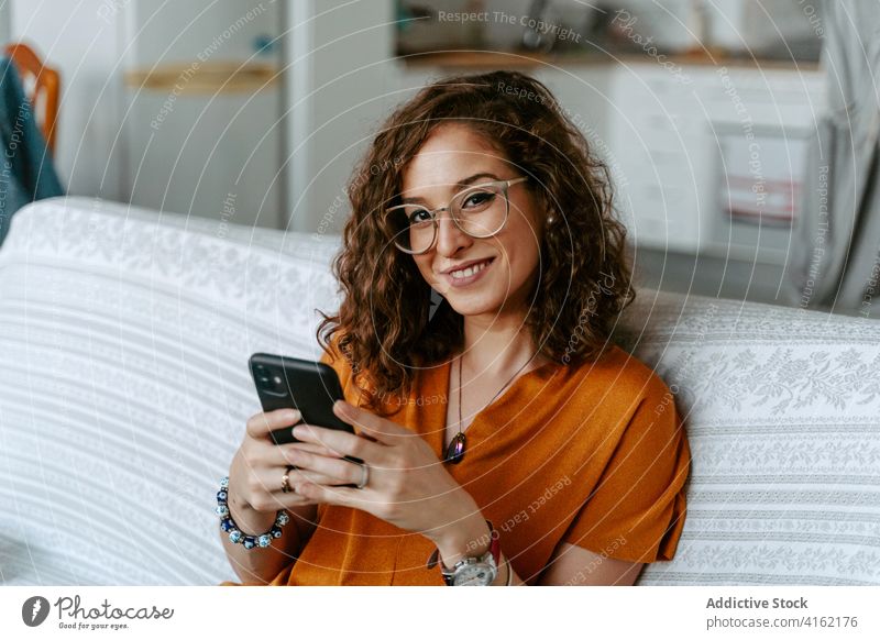 Serious woman browsing smartphone at home rest messaging curly hair concentrate room chill surfing female internet online relax sofa gadget device connection