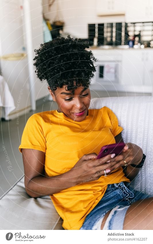 Laughing black woman using smartphone at home laugh having fun excited browsing mobile cheerful millennial young adolescent female modern device gadget