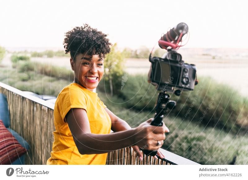 Positive female blogger shooting video on terrace vlog selfie stick camera record cheerful travel happy young woman african american black ethnic excited share